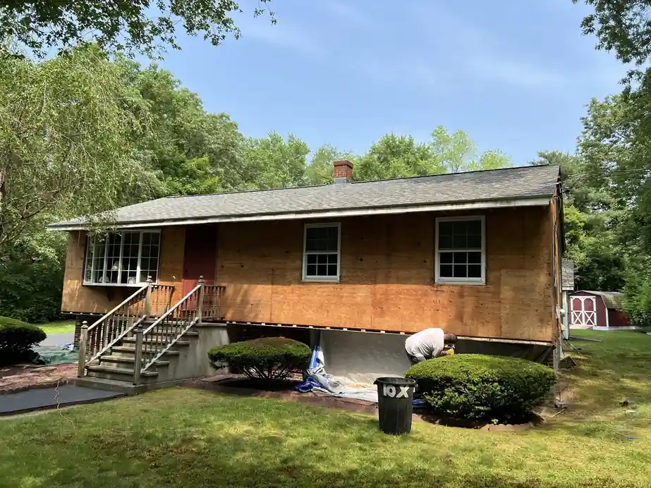 Full siding tear-off to sheathing on a ranch home, worker visible at the foundation line